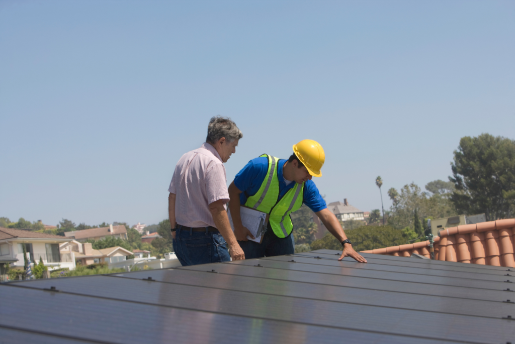 Construction workers inspecting solar panel installation on roof.