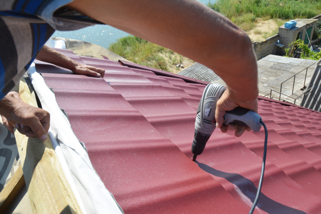 Roofing contractor using a tool to install a red metal roof.