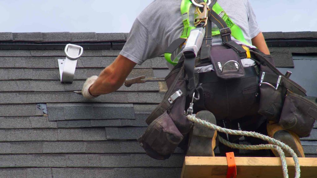 Roofing contractor working on top of a roof strapped into a harness for safety.