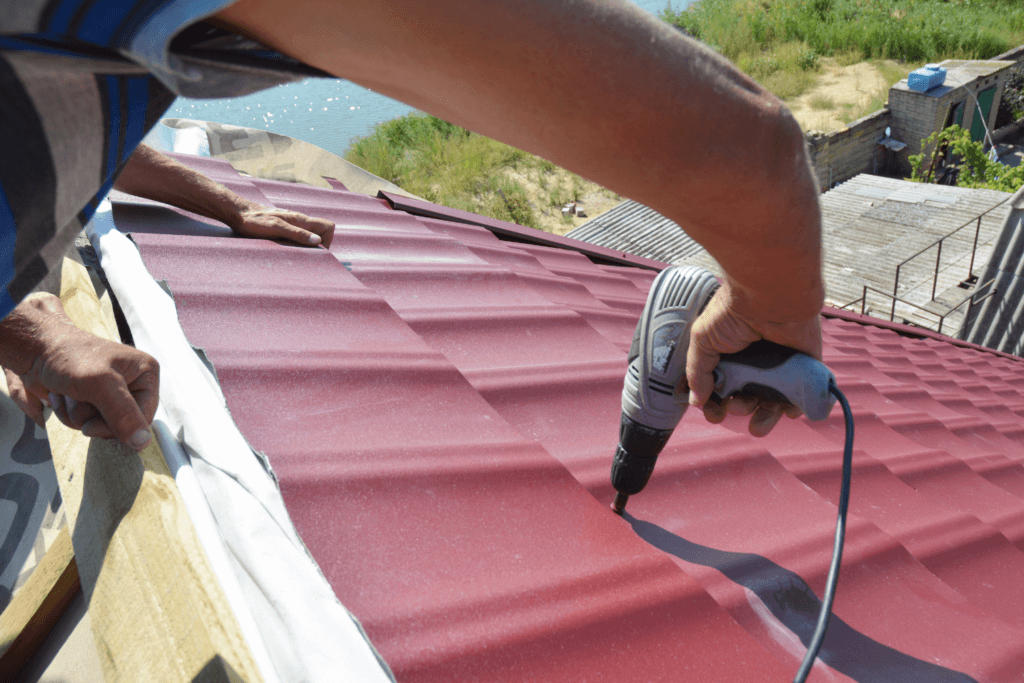 Roofing contractor using a tool to install a red metal roof.